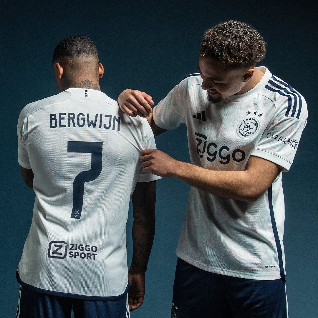 Camisa Reserva do Ajax da temporada 2023/24 Masculina  predominantemente branca e traz um padrão gráfico no corpo, em forma de ondas, inspirado na arquitetura de Amsterdã, com gradiente em turquesa e rosa. Os detalhes do template, como as listras laterais que se juntam na barra, as três listras nos ombros e as três cruzes de Santo André na nuca são azul marinho, enquanto a gola V e os punhos têm a cor branca.  | Tevo Sports